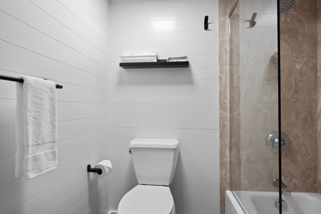 A clean bathroom with a toilet, towel rack, wall shelf, and glass-enclosed shower.