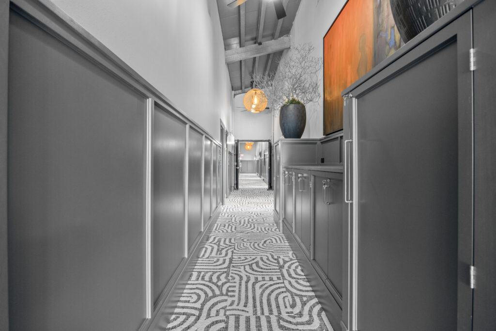 A narrow hallway with gray cabinetry, a patterned runner, and a bright orange accent wall.