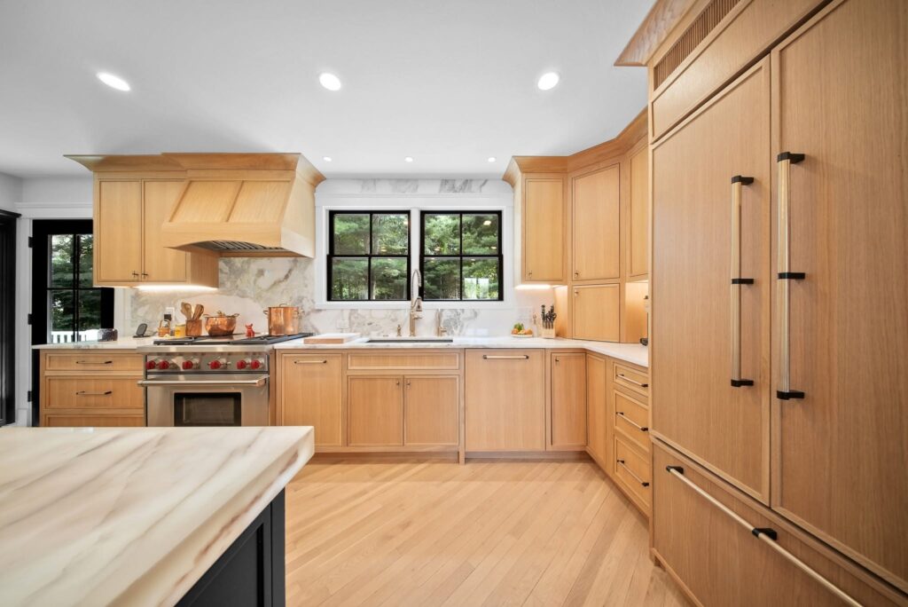 Bright modern kitchen with light wood cabinets, a large island, stainless steel appliances, and windows above the sink.
