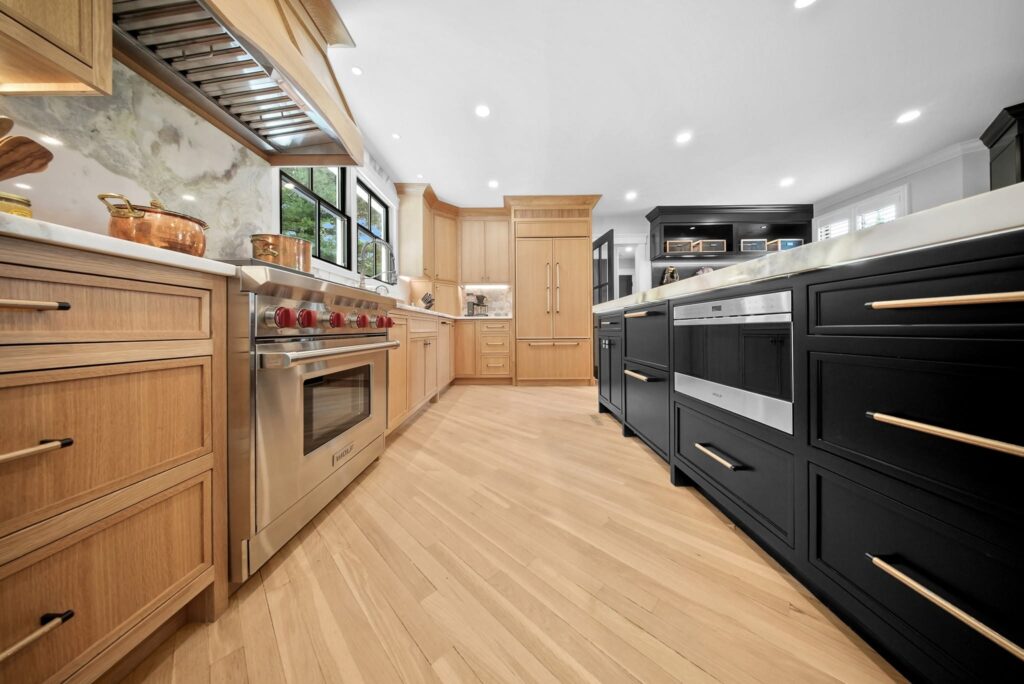 A modern kitchen with light wood cabinets, stainless steel appliances, and a black island.